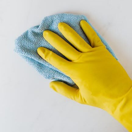 Yellow gloved hand wiping surface with blue cloth, concept of cleaning and hygiene.